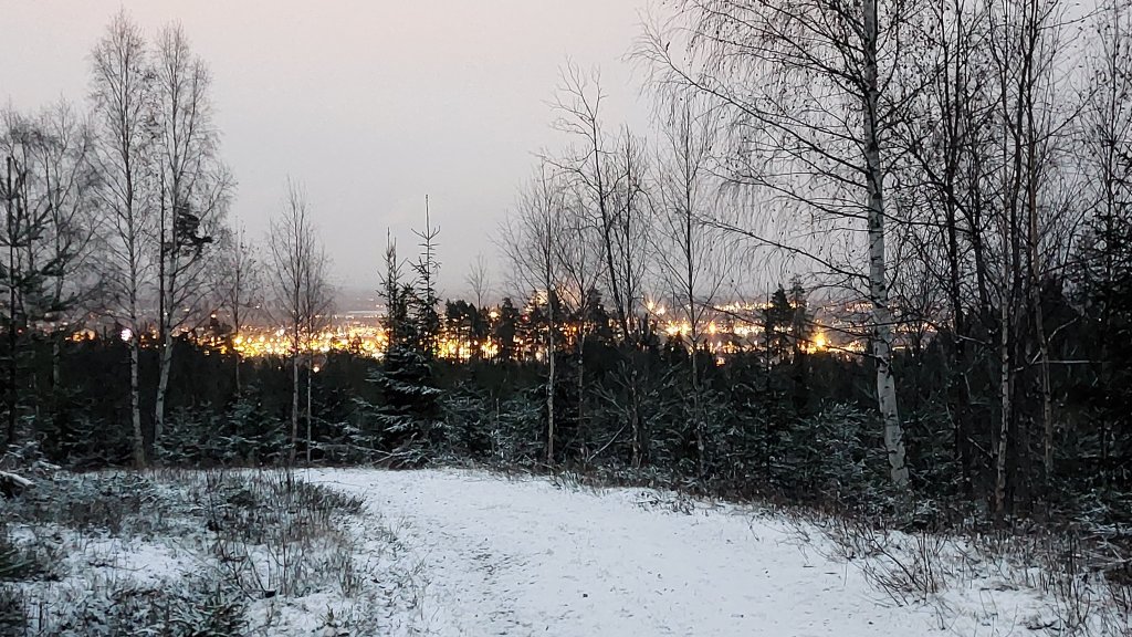 Snowy trail in the evening with a grey sky and a golden glowing landscape in the distance.