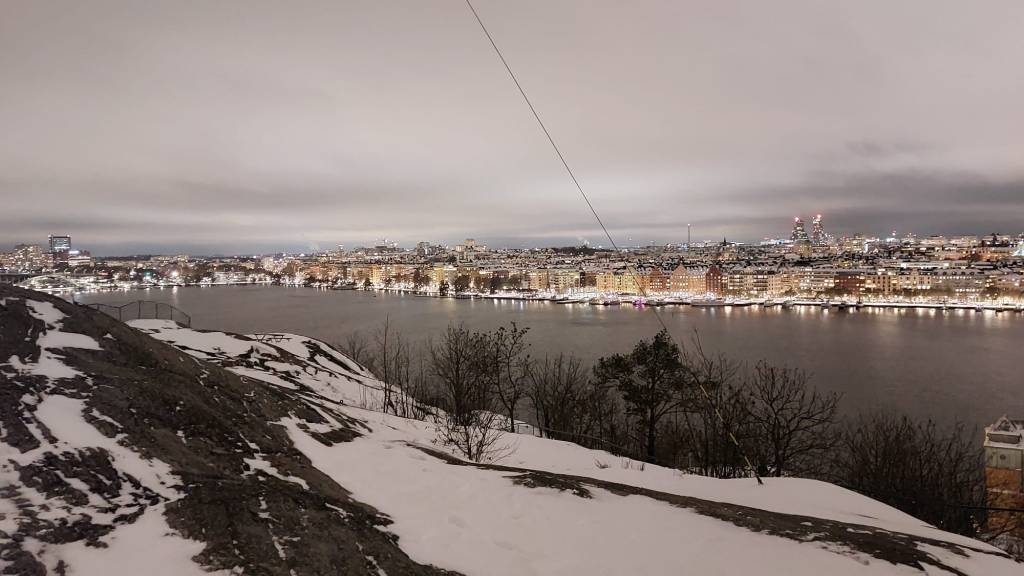 Skyline of Stockholm with a cloudy, grey sky. On the bottom of the picture are a wide river stone ground covered in snow.